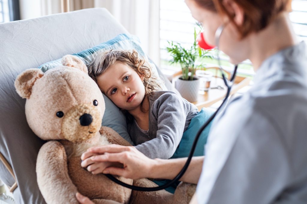 Friendly female doctor examining small girl in bed in hospital.