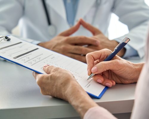 Closeup older patient filling medical heath data form in hospital clinic.