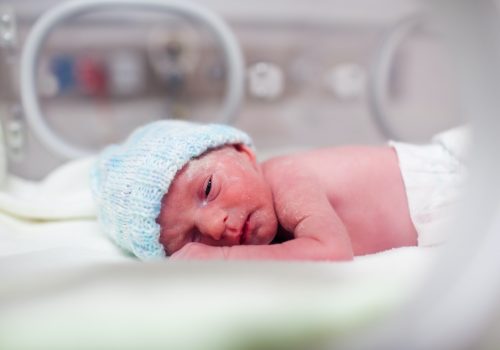 Newborn boy covered in vertix in incubator